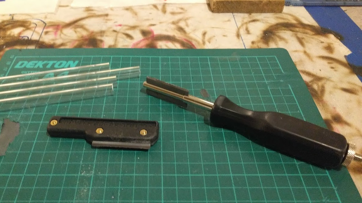 tungsten carbide knife scoring a glass tube with single clean scratch, close-up view